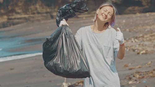 Un voluntario en una playa del Océano Negro con basura de plástico en una bolsa negra muestra un letrero en forma de mano