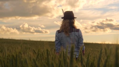 young caucasian bohemian female wearing hat in a barley field during sunset