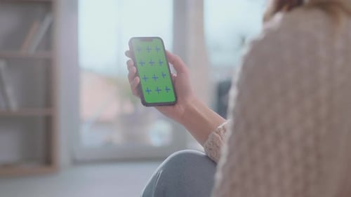 Woman Holds Smartphone with Green Screen Indoors