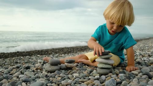 Little Boy Builds a Tower of Stones on the Seashore