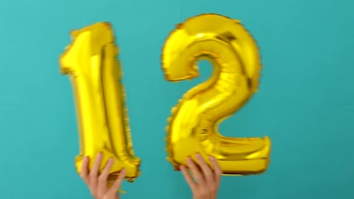 Hands Hold Gold Number Twelve Foil Balloons