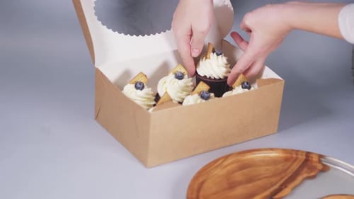 Hands of a Young Woman Pack Cupcakes in a Craft Box with a Ribbon Bow