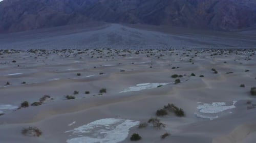 Tilting shot revealing giant mountain in the desert. Sand dunes in the foreground. Drone video