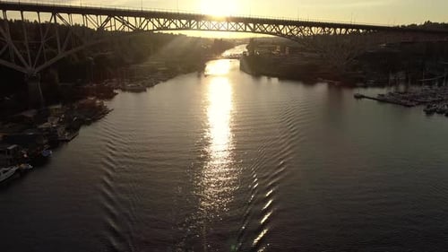 Aerial Passing Over Boats In Canal With Sun Rays Shining In Big City Bridge Rafters