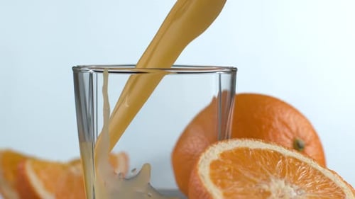 Orange Juice Pouring Into Glass Next to Fruit