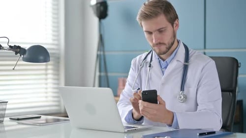 Doctor Using Smartphone While Working on Laptop in Clinic