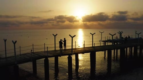 Aerial Fly Over Pier with Couple Making Selfies Against the Sunrise Silhouette