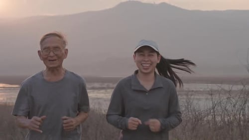 Grandfather and granddaughter are jogging by the lake at sunset and tell stories of past life experi