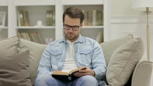 Adult Man Reading Book on Couch Indoors