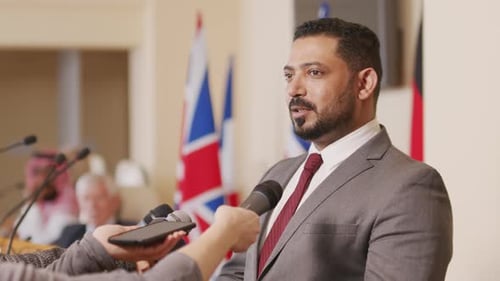 Man Speaking at a Press Conference with Flags