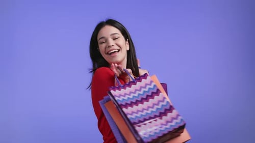 Excited Woman with Colorful Paper Bags After Shopping on Violet Studio Background