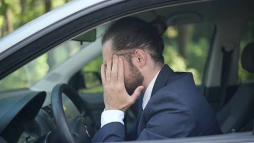 Side View Portrait of Young Stressed Caucasian Man in Suit Sitting on Driver's Seat Rubbing Temples