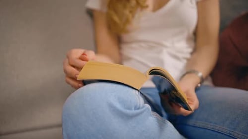 Nahaufnahme Frau liest Buch und blättert Seite um, wenn sie auf dem Sofa sitzt