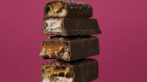 Vier Schokoriegel drehen sich auf rosafarbenem Hintergrund. Makroaufnahme der unverpackten Süßigkeiten in Nahaufnahme. Nougat und Karamell