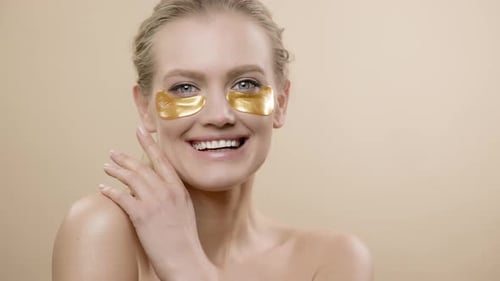 Woman Applies Golden Eye Patches and Smiles