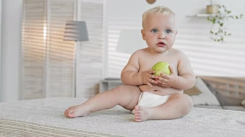 Adorable Infant Eating a Green Apple on Bed