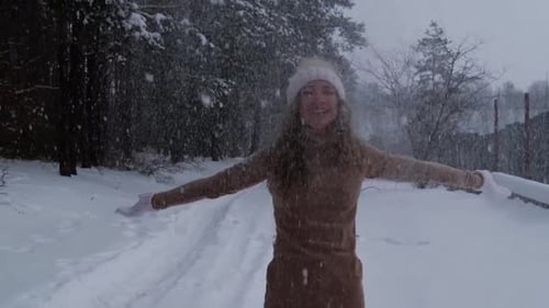 Woman Enjoying Winter Snowfall with Arms Outstretched
