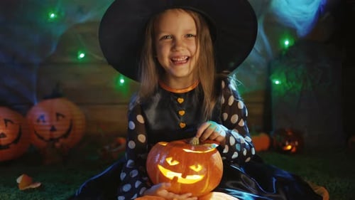 Smiling Girl in Witch Costume Holding Jack-o'-Lantern
