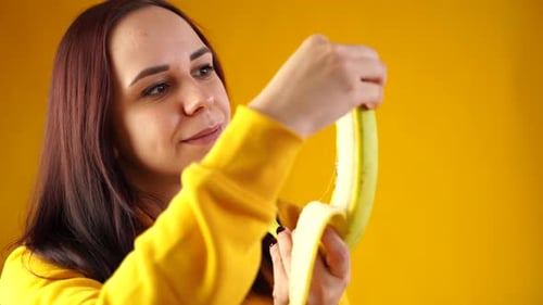 Close Up of Young Woman Peeling Banana on Yellow Background