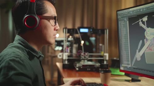 Asian Engineer Start Work On Personal Computer And 3D Printer, Screen Shows 3D Drone Delivery