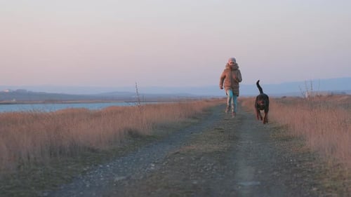 Une fille en veste court et s'amuse sur la plage au bord de la mer avec un chien Rottweiler