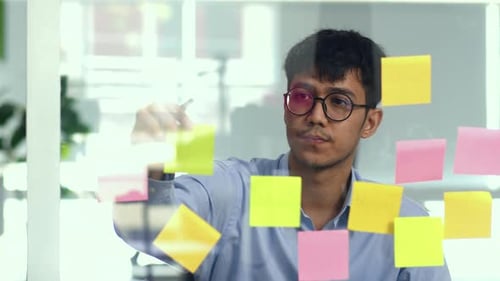 Young Adult Writing on Glass Board in Office