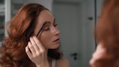 Woman Brushing Eyebrows in Bathroom Mirror