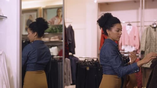 Beautiful African American Woman Choosing Clothes Hanging on Hangers in Trendy Clothing Store