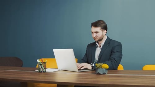 Joven barbudo, programador, apariencia caucásica, sentado y trabajando en un ordenador portátil