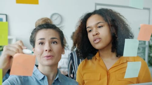 Women Collaborate and Brainstorm on Glass Whiteboard