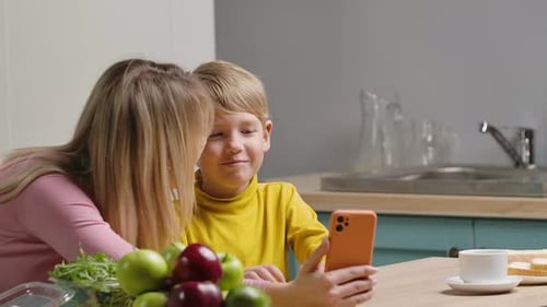 Mother and Son Chatting on Mobile Phone in Kitchen