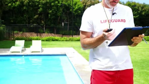 Lifeguard Standing Poolside Reviewing Clipboard on Sunny Day