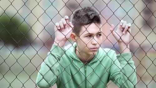 Teenager Stands Behind a Fence with Pensive Mood