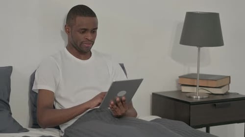 Young Man Using Tablet in Bed Indoors
