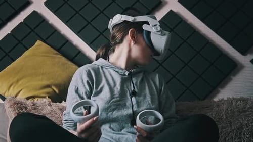 Young Woman in Virtual Reality Helmet Sitting on Sofa and Move Hands at Home