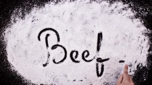 Hand Writes the Word Beef in White Powder