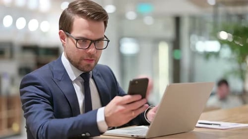 Professional Man Using Phone and Laptop at Desk