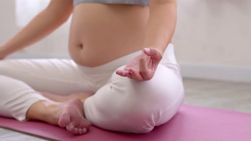 Close up Pregnant Woman sit on yoga mat and doing yoga lotus pose at cozy home