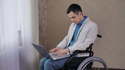 Man in Wheelchair Works on Laptop Indoors