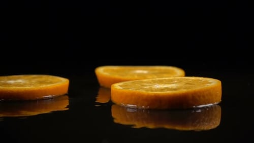 Orange Slices Fall on the Black Surface Covered with Water