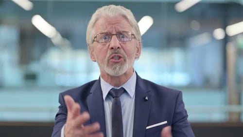 Angry Senior Man in Office Talking to Camera