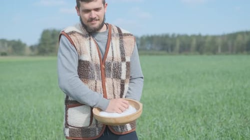 A Young Peasant Man Is Sowing the Field with Grain at a Village. A Farm Concept