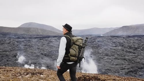 Photographer Walking And Sitting On Rock By Lava Field