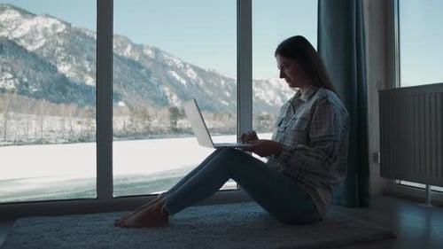 A Woman Works at Home Sitting Near the Window Using a Laptop
