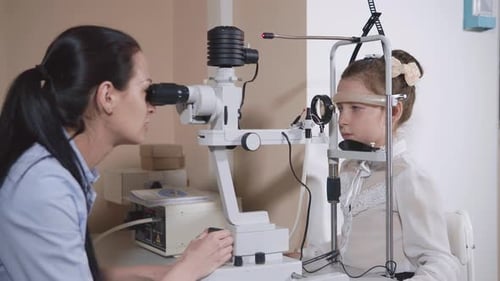 Woman Optician Is Examining Eyes of Little Girl in a Medical Office
