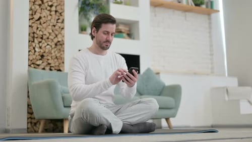 Young Adult Using Smartphone on Yoga Mat Indoors