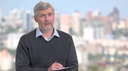 Man Writing on Clipboard in Front of City