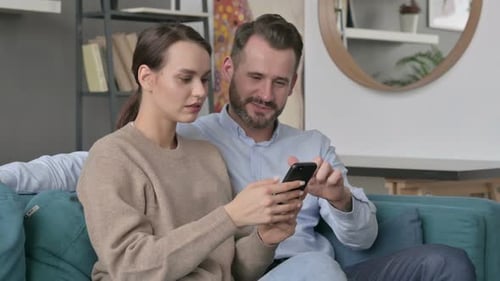 Cheerful Couple Relaxing at Home, Looking at Smartphone
