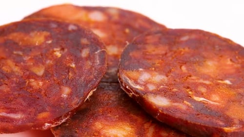 Spanish intense red chorizo sausage slices. Close up macro shot with rotation and white background.