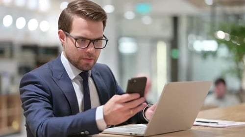 Business Man Works on Laptop with Phone at Desk